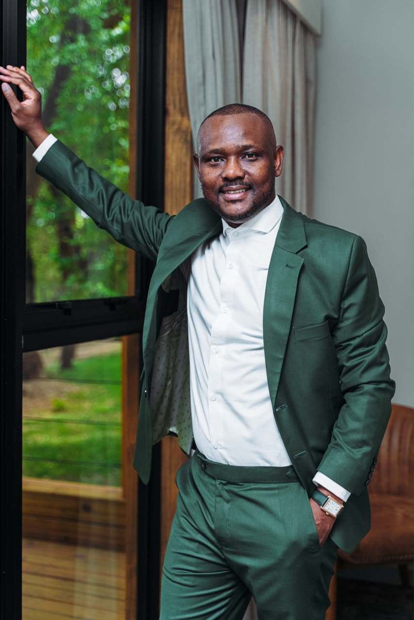 Mothusi Molokomme standing beside a window in a green suit.