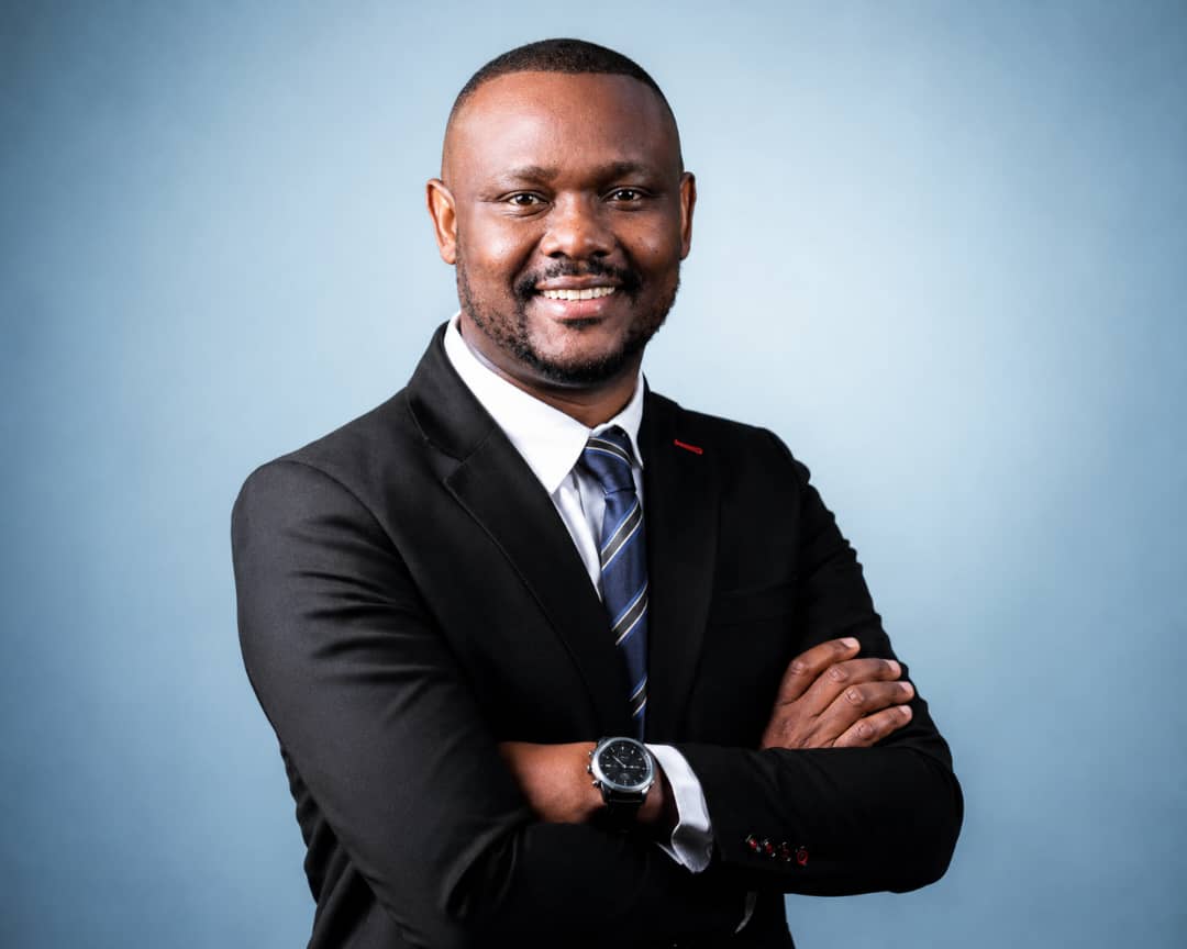 Mothusi Molokomme in a dark suit, smiling with his arms folded.